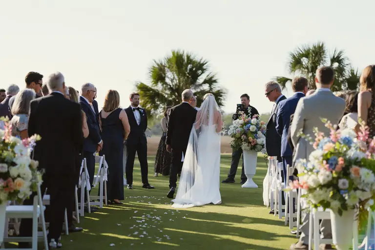 Guests standing as the ceremony begins beneath the palms