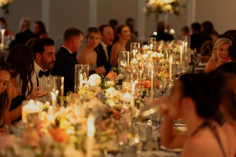 Guests around a candlelit reception table dressed with flowers