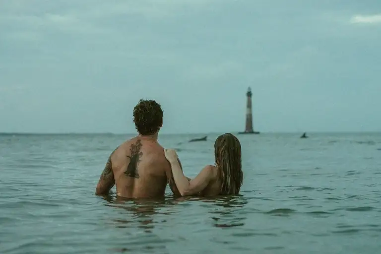 Couple wading into the ocean toward a distant lighthouse