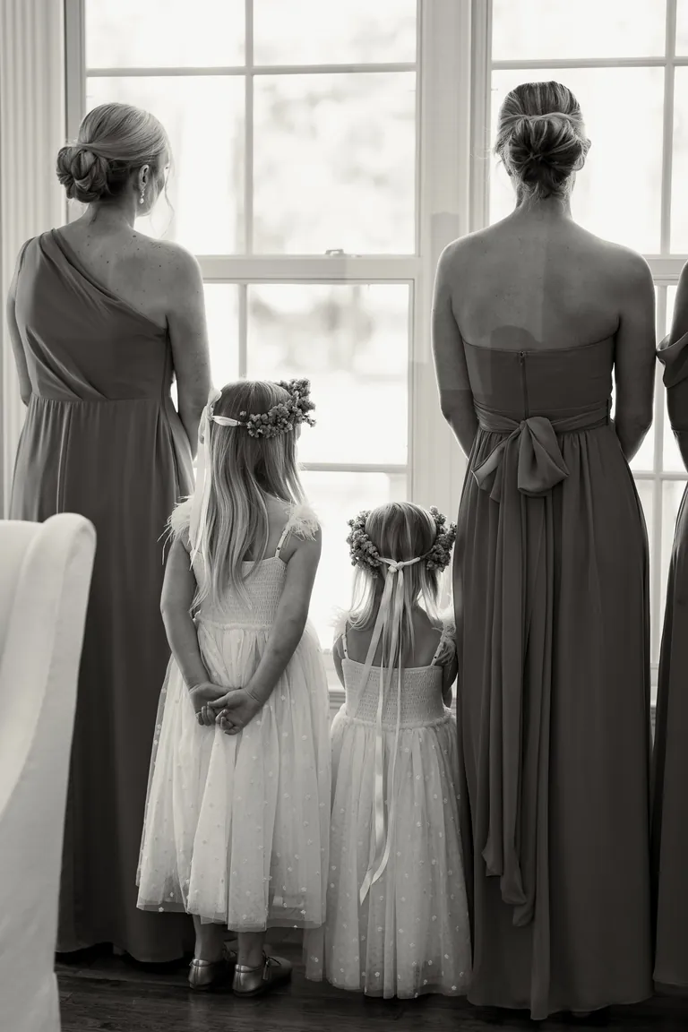 The bridal party and flower girls watching from the window, black and white