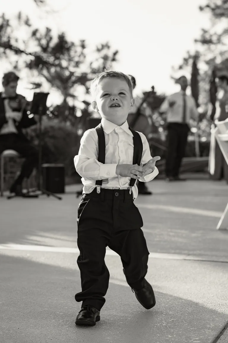 A little boy in suspenders walking across the dance floor, black and white