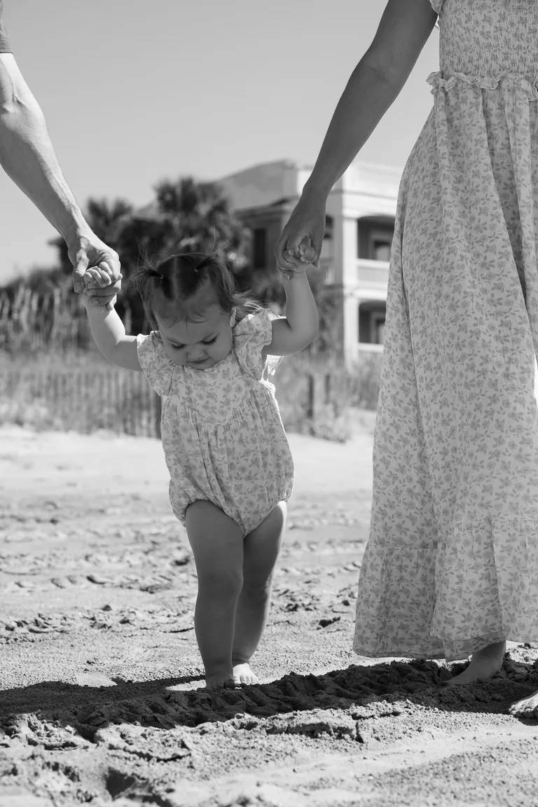 A child in a sunhat running across the sand hand in hand with her mother, black and white
