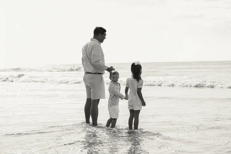A family of four holding hands in the shallow surf, black and white