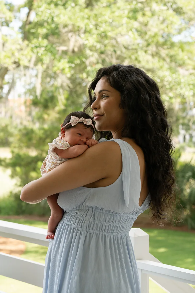 A mother in a blue dress holding her newborn on the porch