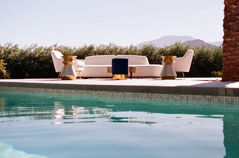 A swimming pool framed by pale lounge furniture and desert mountains