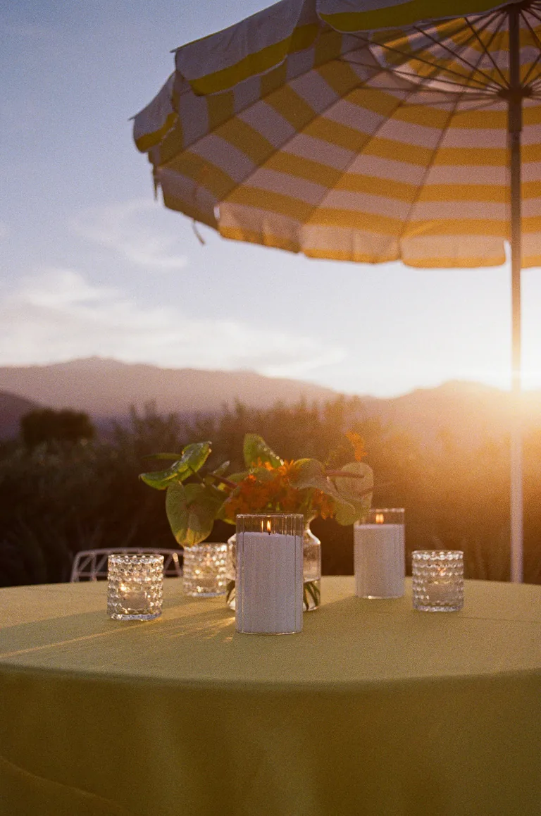 A table laid under a striped umbrella as the sun sets over the mountains