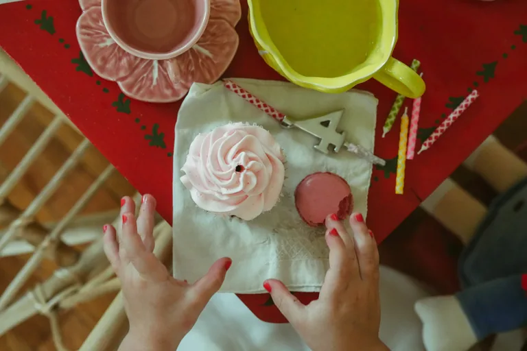 Small hands decorating party favours at a red craft table