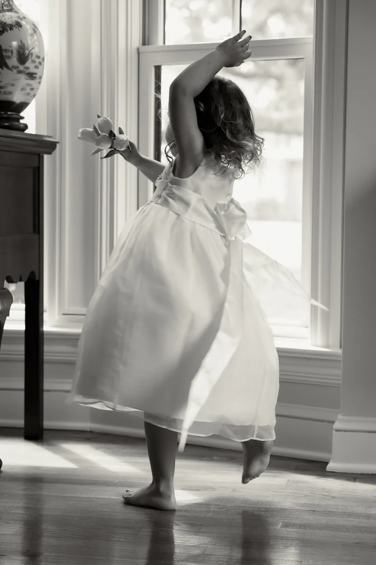 A girl twirling in her party dress in a sunlit doorway, black and white
