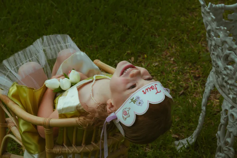 A baby in a bonnet lying in a wicker cradle on the grass