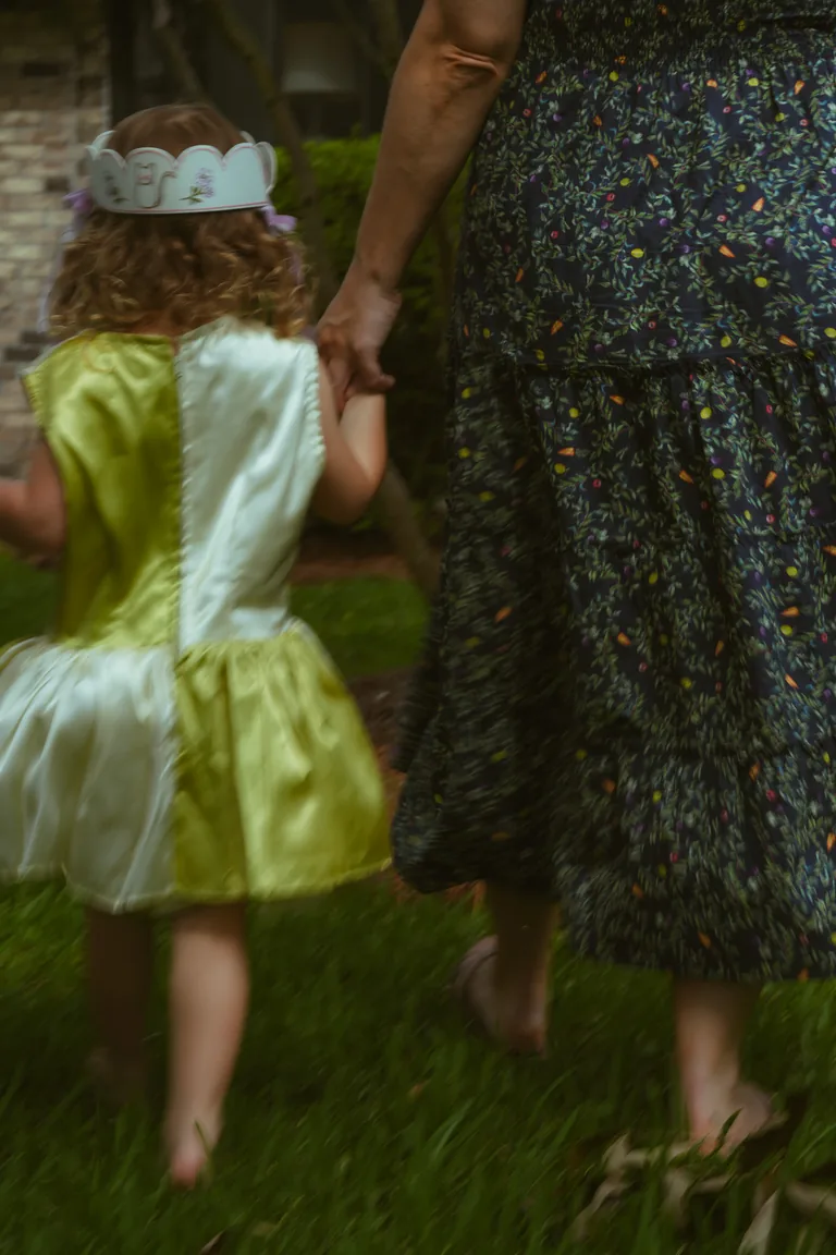 A girl in a yellow dress walking across the lawn beside her mother