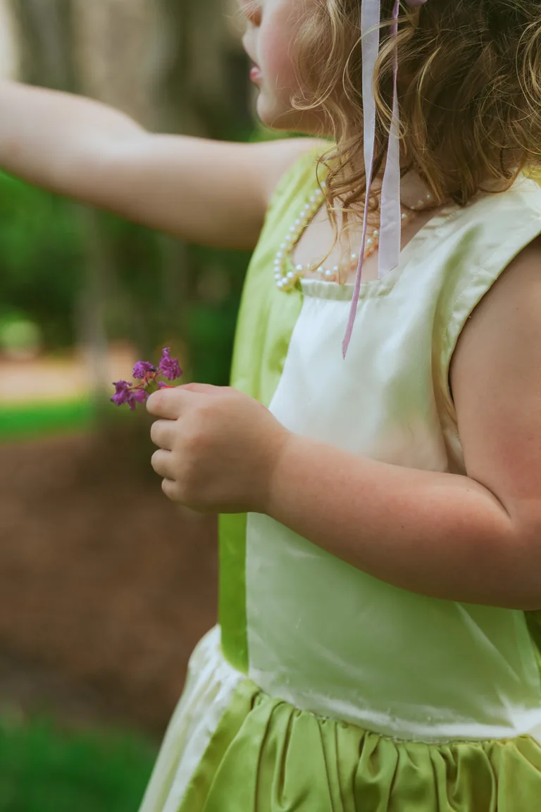 A girl in a pale green dress holding a handful of purple wildflowers