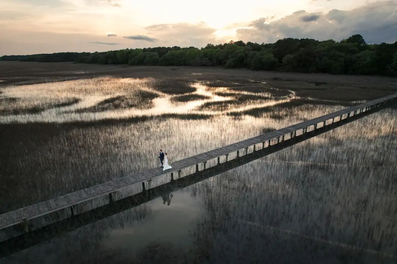 Aerial view of a couple on a marsh boardwalk at sunset